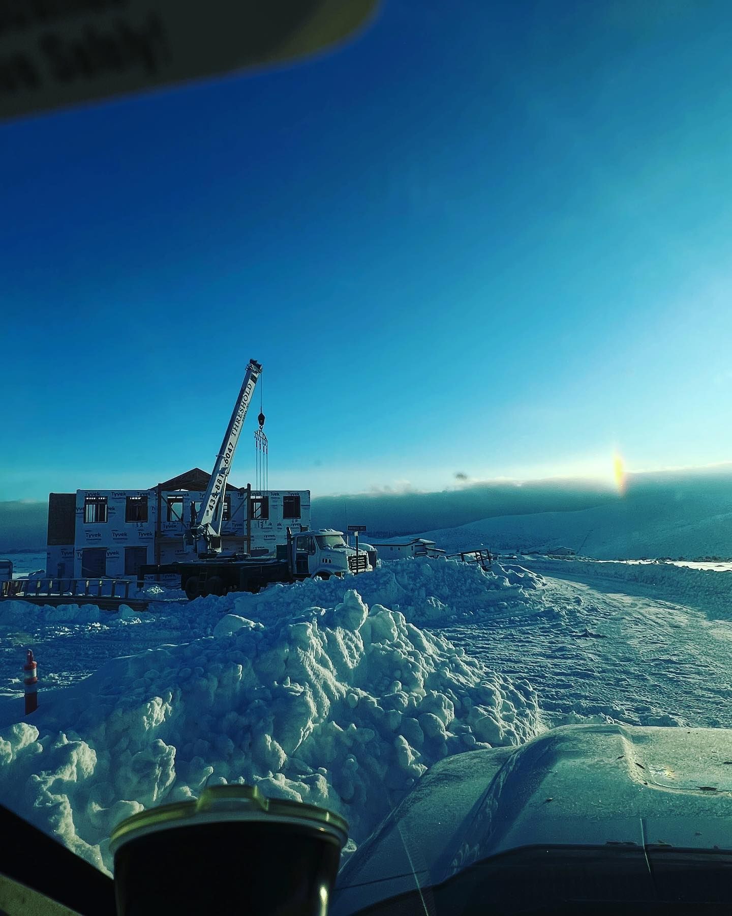 Construction site with crane, partially built structure, and snow-covered ground under a clear, bright sky.