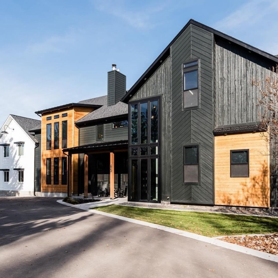 Modern multi-level home with dark gray and wood siding, glass door, and a black chimney.