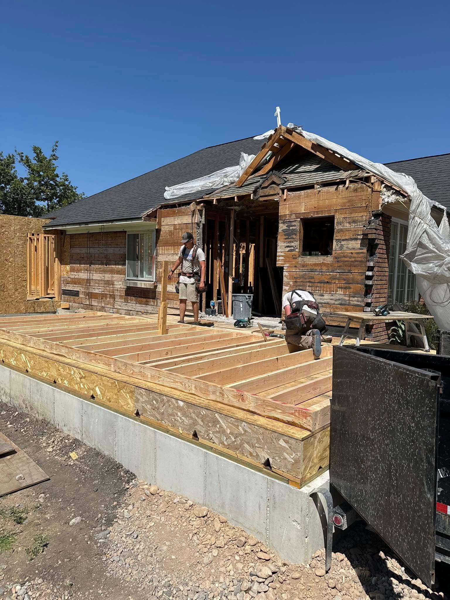 Construction site. Partially deconstructed house with workers on a new wooden deck in front. Blue sky.