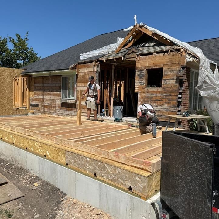 House under construction; workers on a new deck, exposed wooden frame and demolition progress.