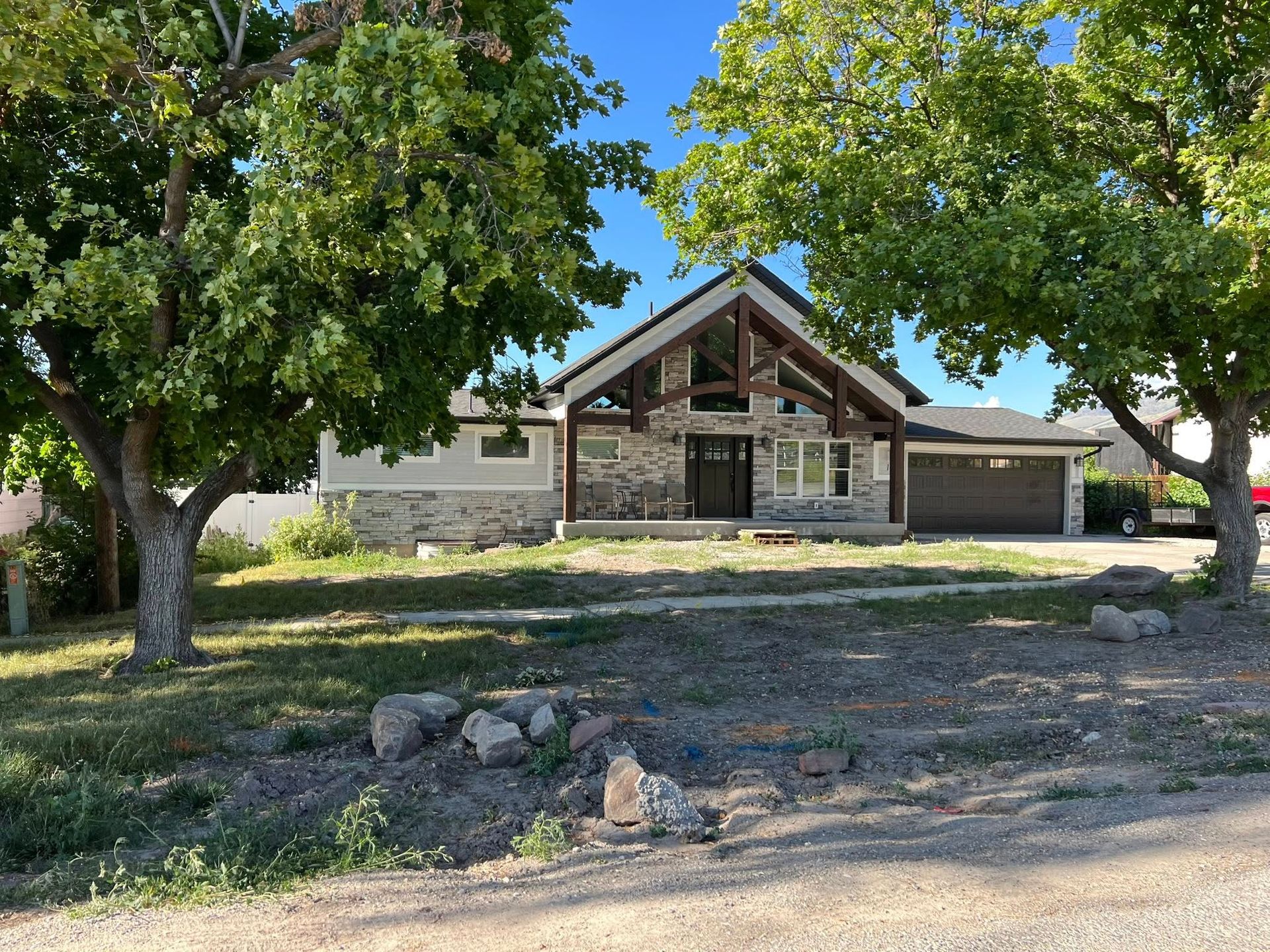 House with stone and wood exterior, flanked by trees, on a sunny day.