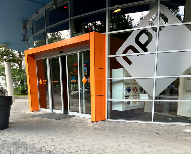 Moderne pui met oranje deurkozijn, glazen deuren en een witte rastergevel aan de stoep.