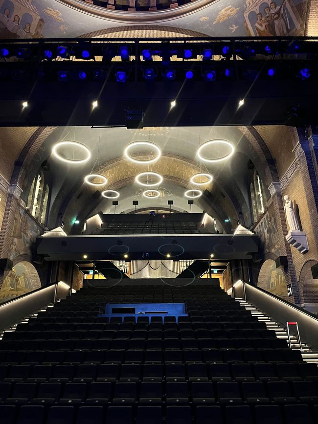 Modern auditoriuminterieur met ringverlichting en rijen stoelen in een donkere, rijkversierde ruimte.