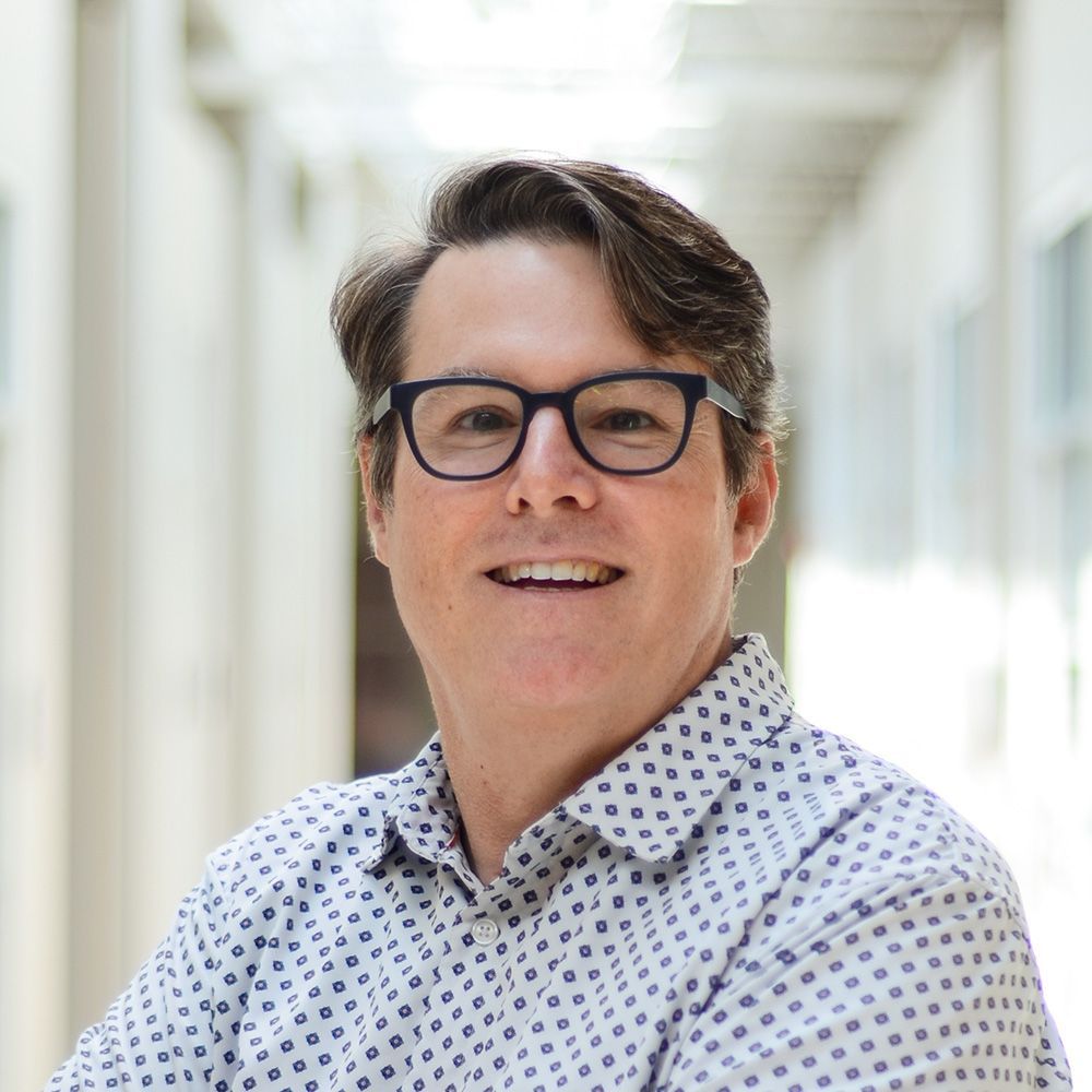 A black and white photo of a man wearing glasses and a polka dot shirt.