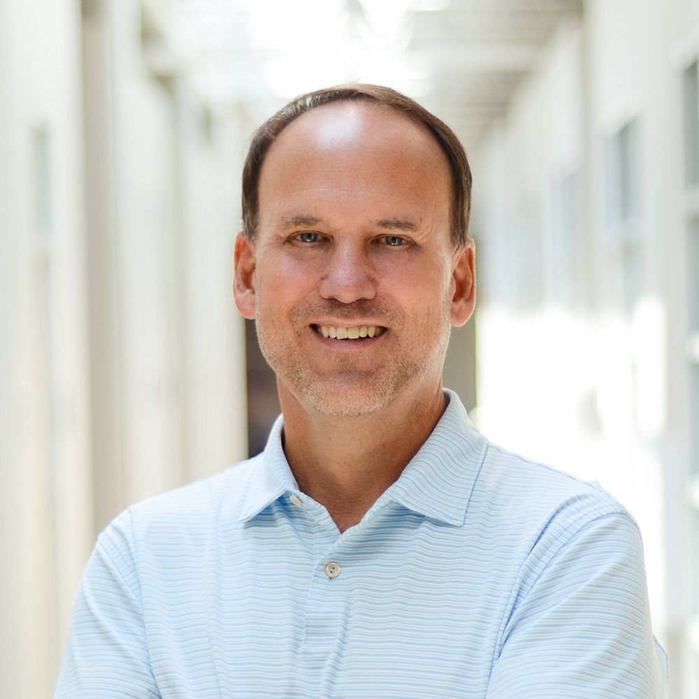 A man in a plaid shirt is smiling in a black and white photo.