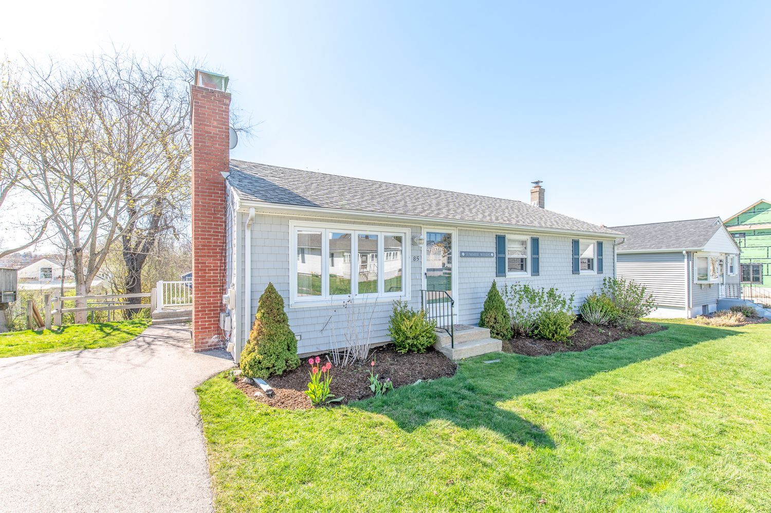 A white house with a brick chimney and a large lawn in front of it.