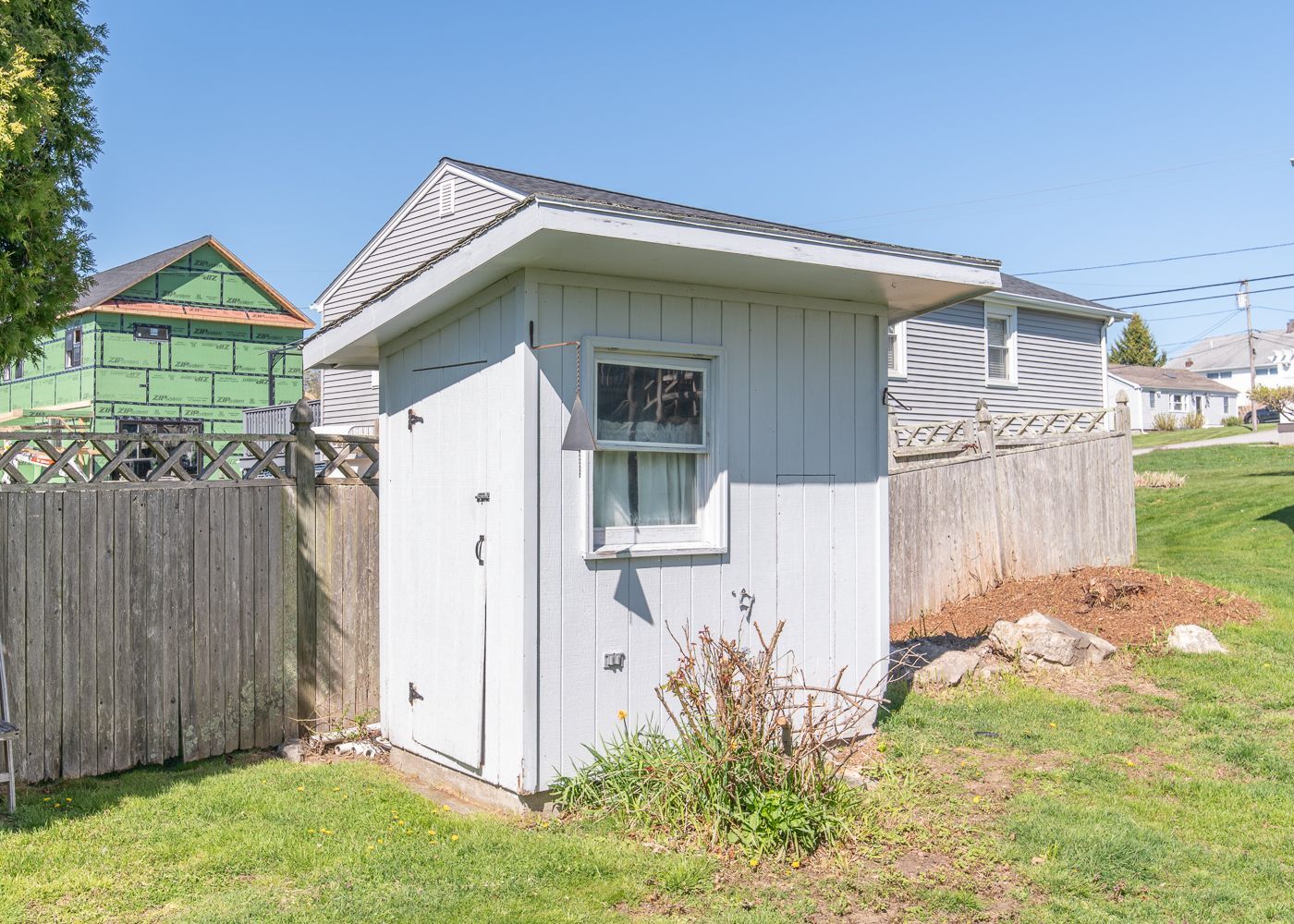 A small white shed with a window in the backyard of a house.