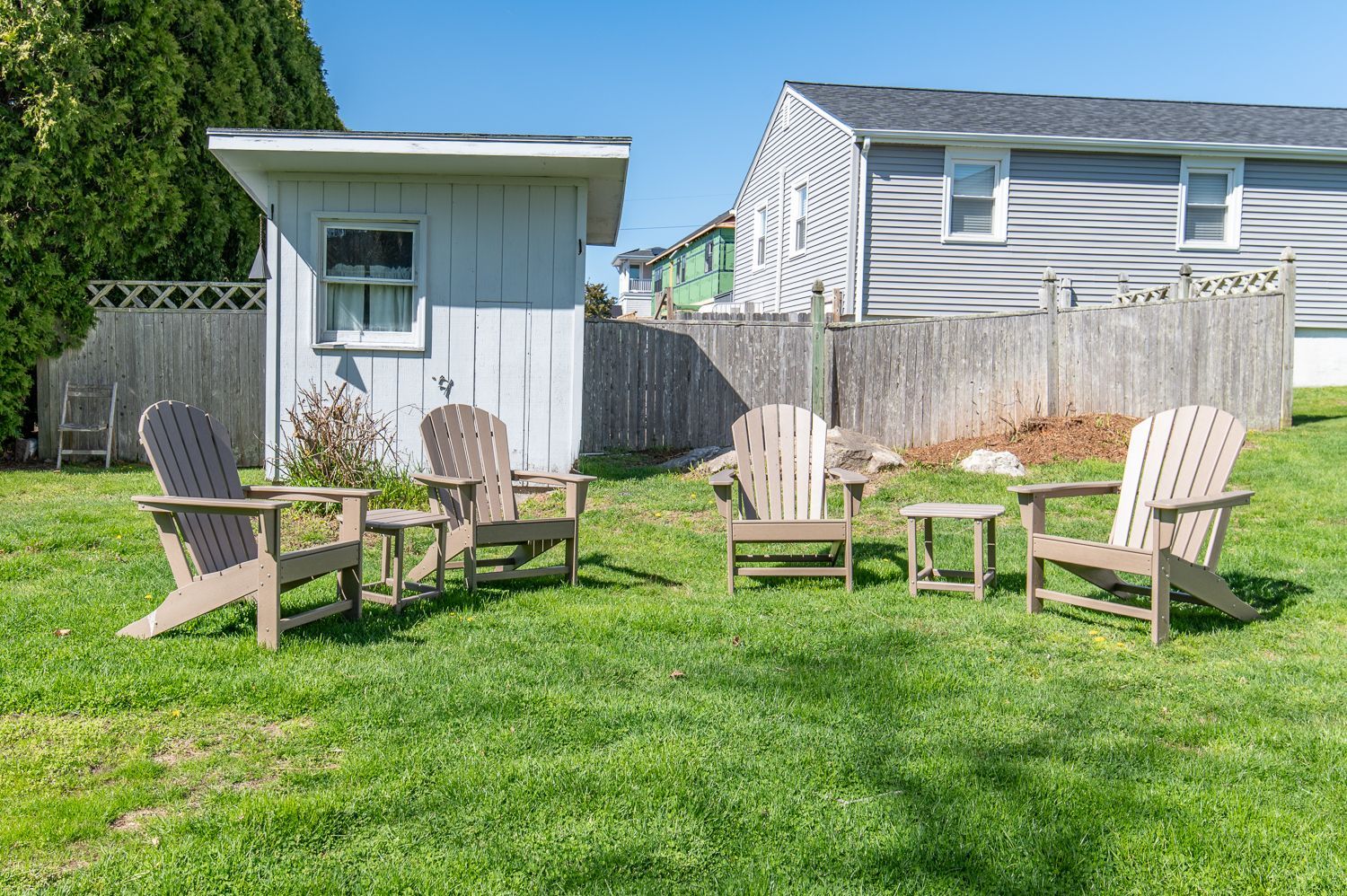 A group of wooden chairs are sitting in a grassy yard in front of a house.