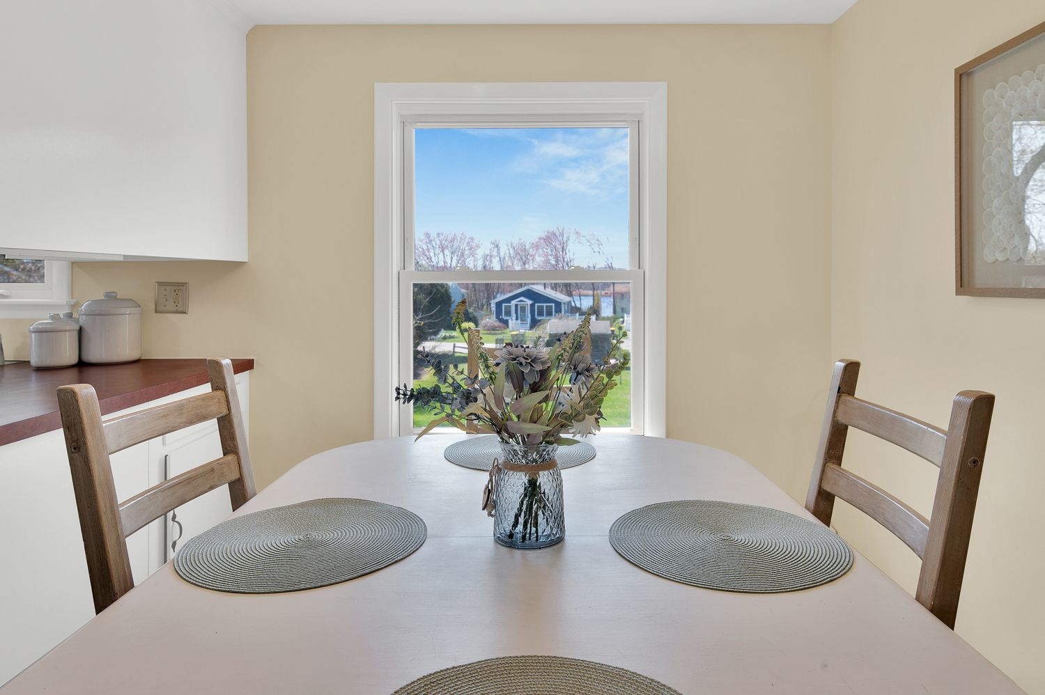 A dining room table with a vase of flowers on it in front of a window.