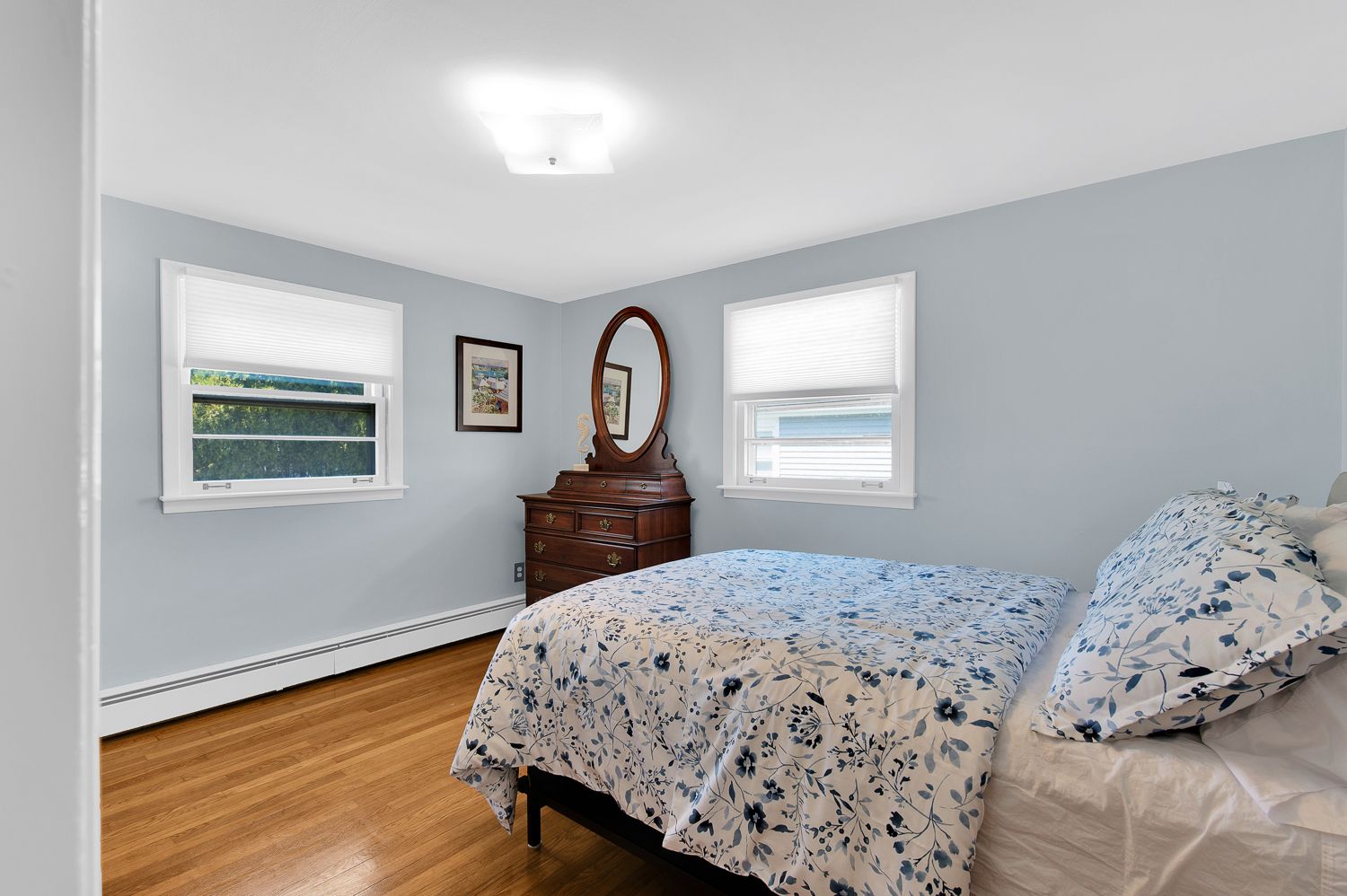 A bedroom with a bed , dresser , mirror and two windows.
