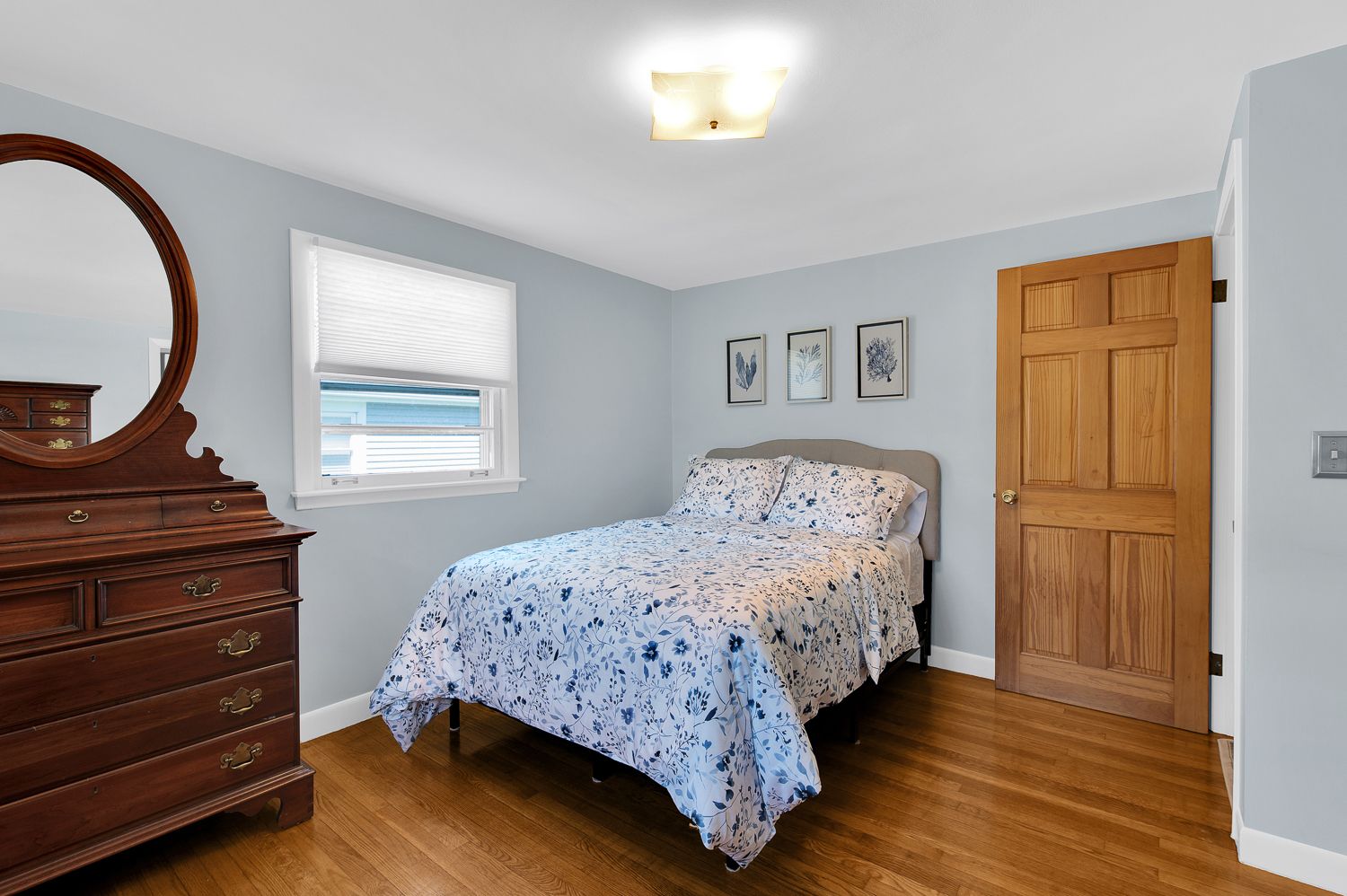 A bedroom with a bed , dresser , mirror and window.