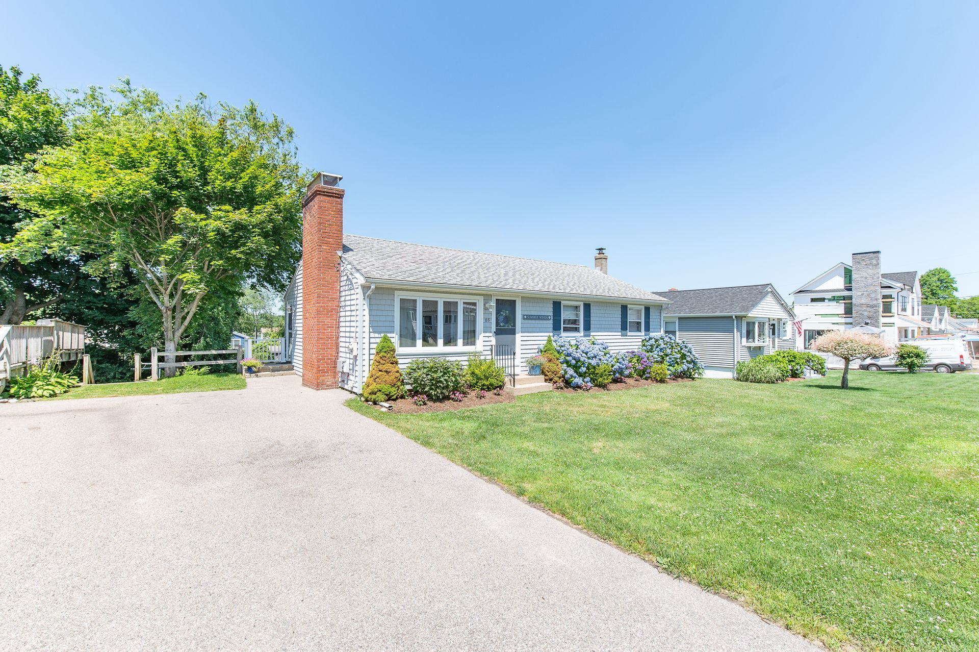 A white house with a brick chimney is sitting on top of a lush green lawn.
