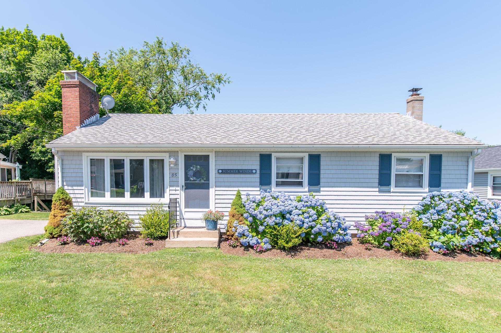 A white house with blue shutters is sitting on top of a lush green lawn.