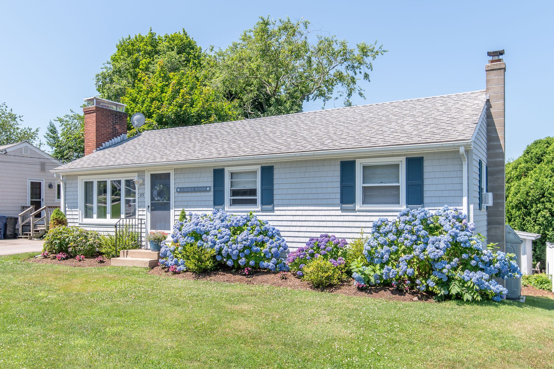 A white house with a brick chimney and blue shutters on a snowy day.