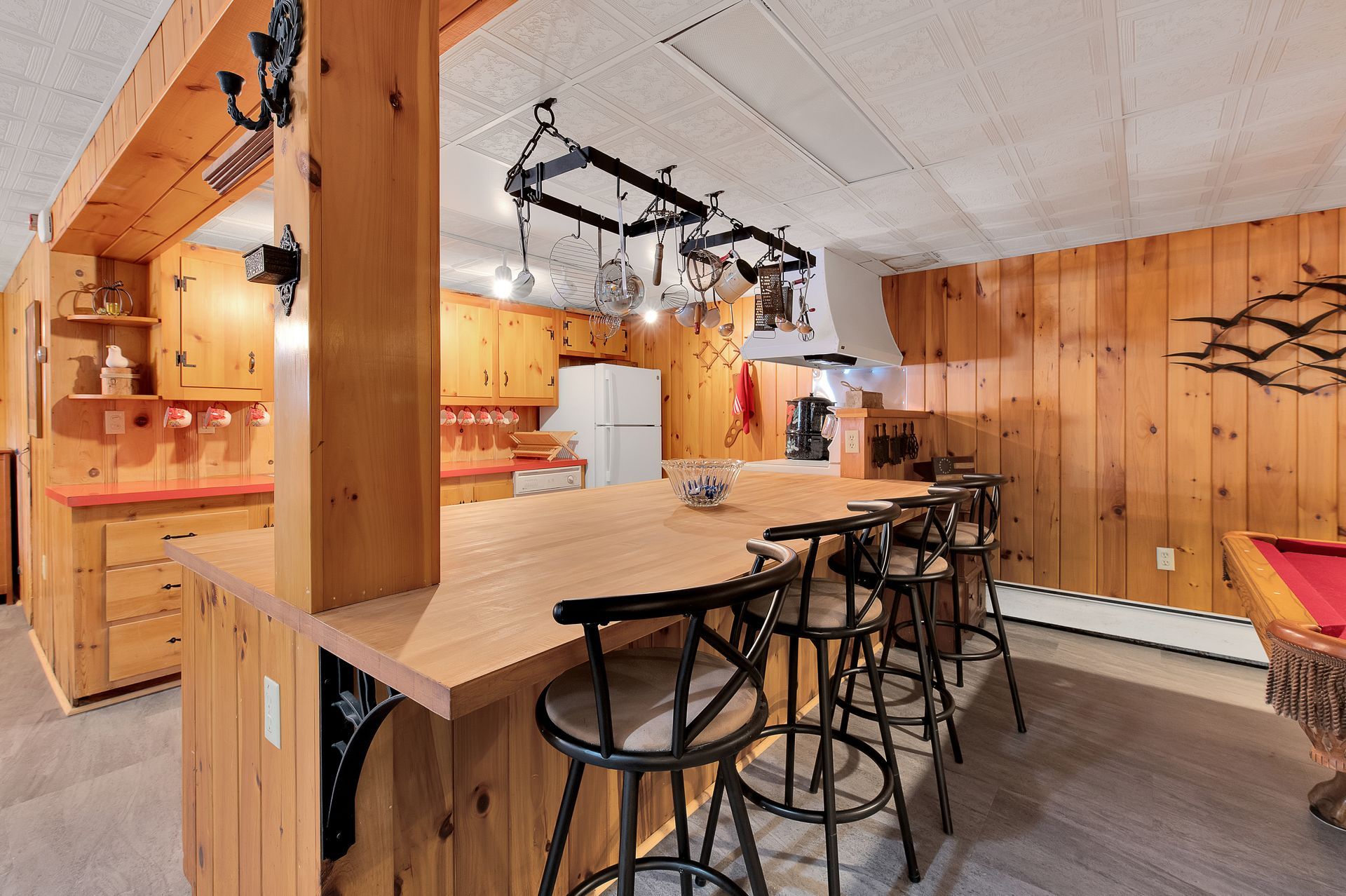 A kitchen with a bar and stools and a pool table