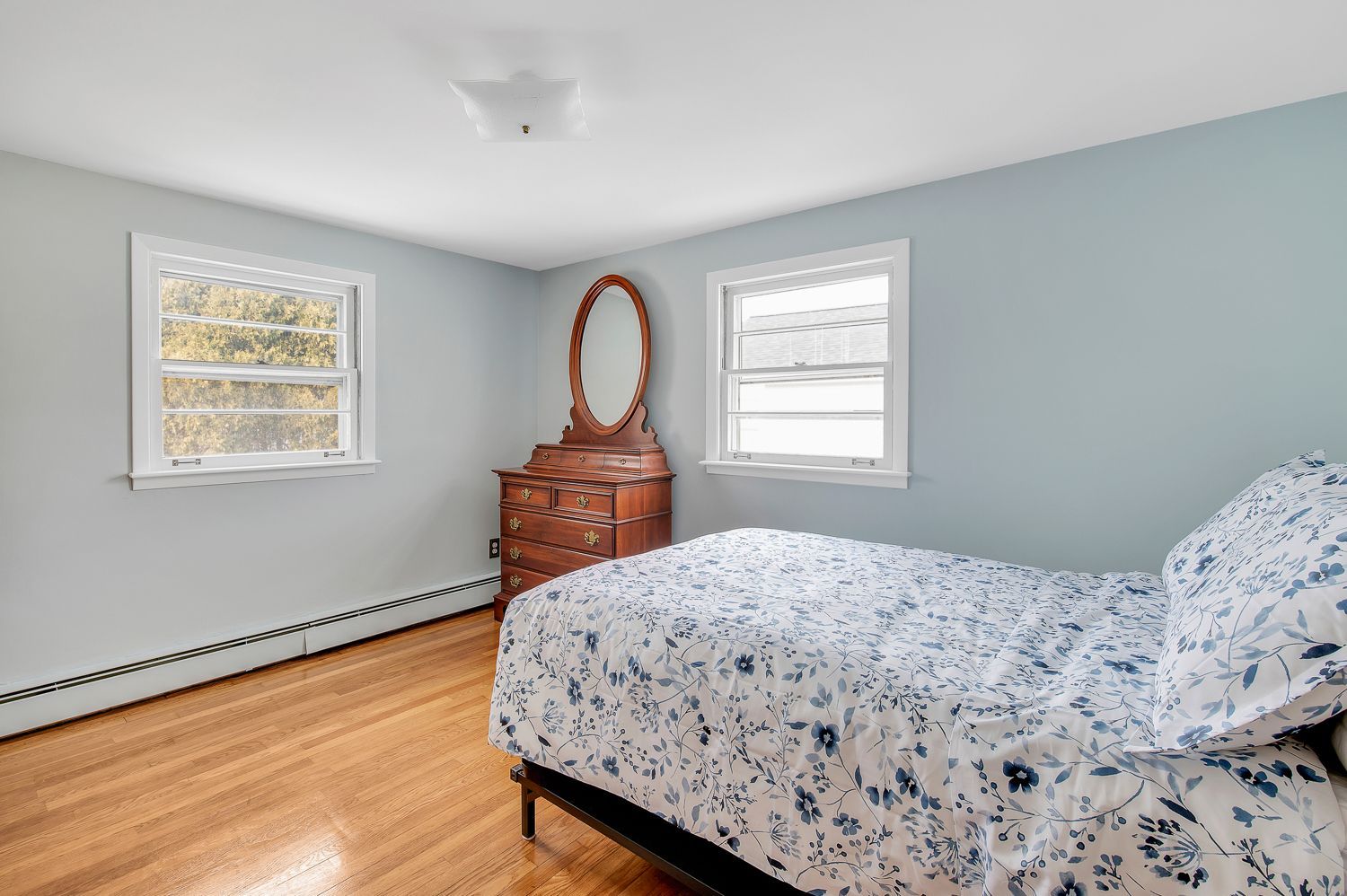 A bedroom with a bed , dresser , mirror and two windows.