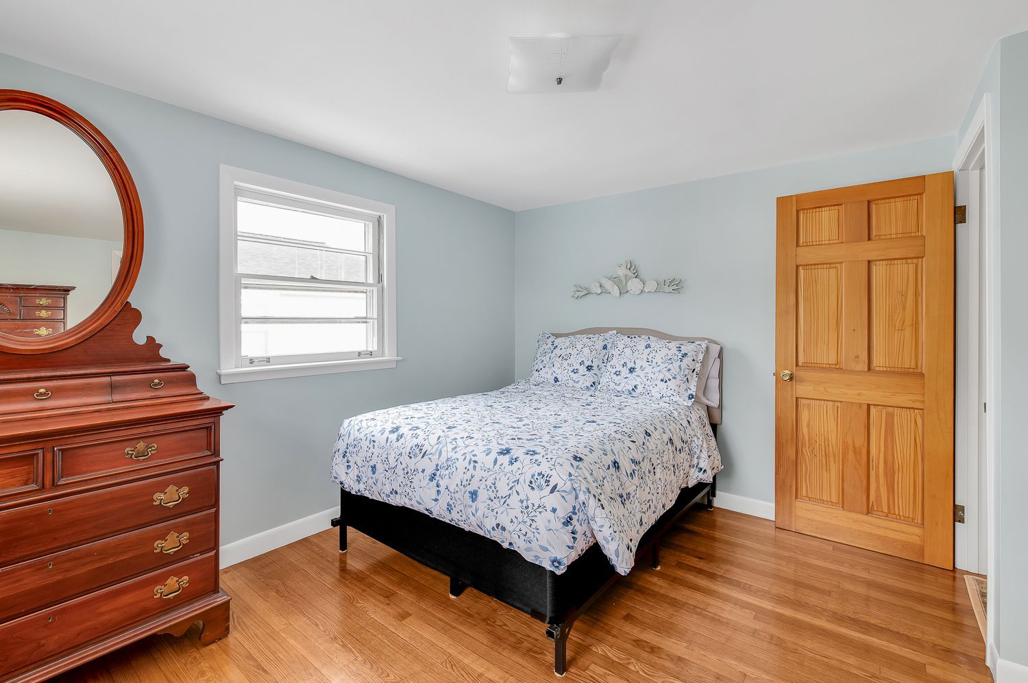 A bedroom with a bed , dresser , mirror and window.