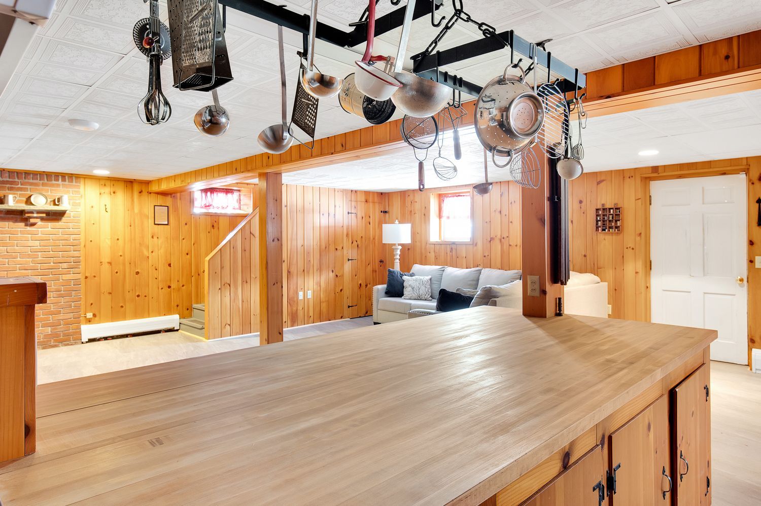 A kitchen with a wooden counter top and pots and pans hanging from the ceiling.