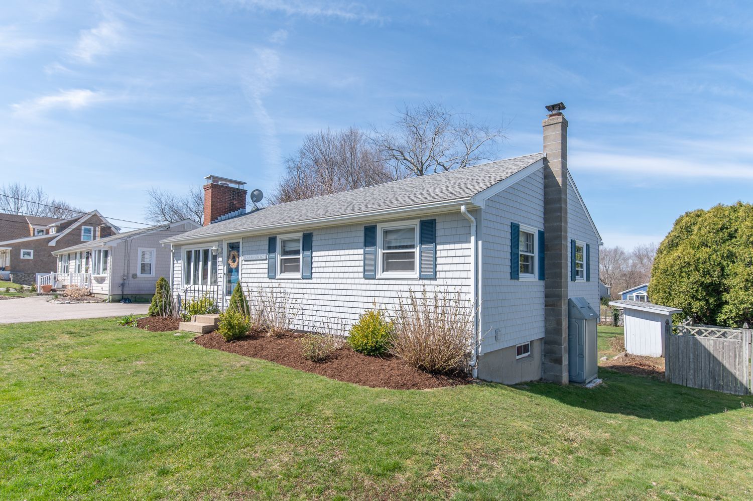 A white house with blue shutters is sitting on top of a lush green field.