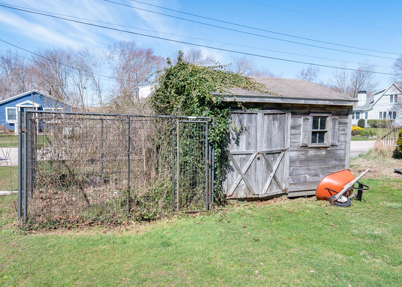 A wooden shed with a wheelbarrow in front of it in a yard.