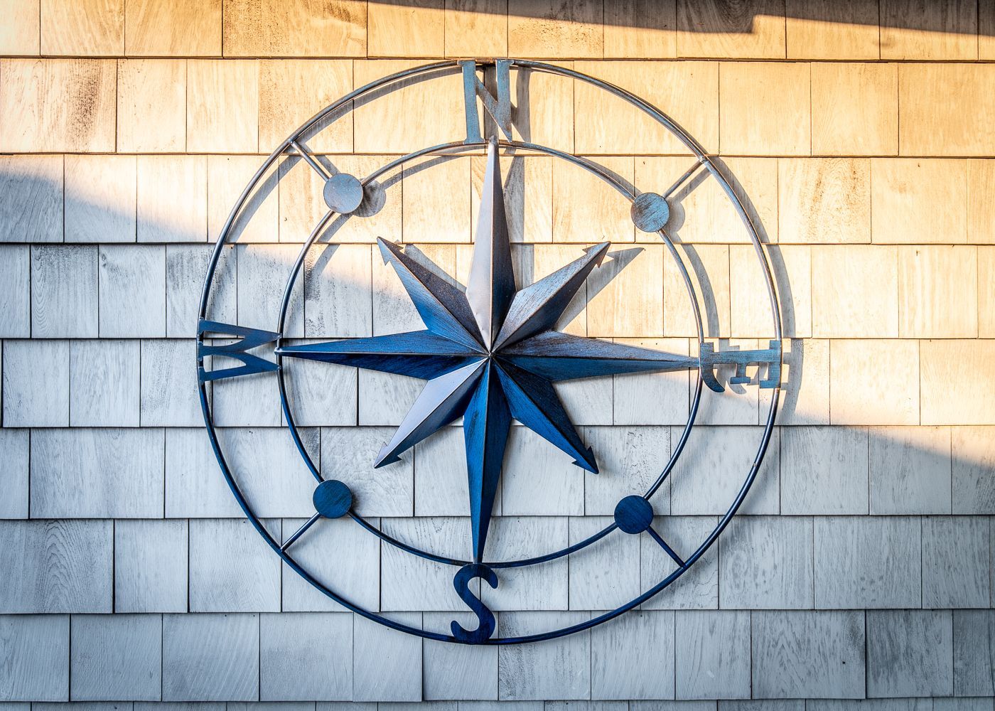 A blue and white compass is hanging on a brick wall.