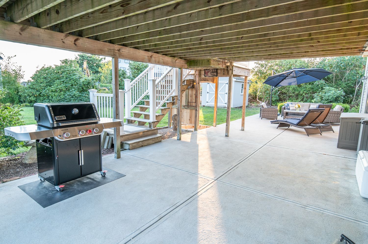 A patio with a grill and umbrella under a wooden deck.