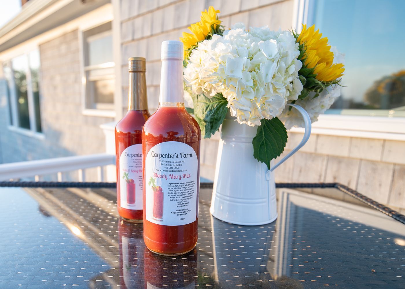 Two bottles of tomato juice are on a table next to a vase of flowers