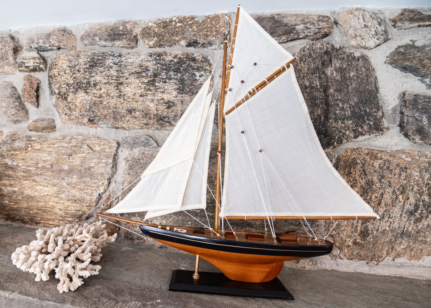 A model sailboat is sitting in front of a stone wall
