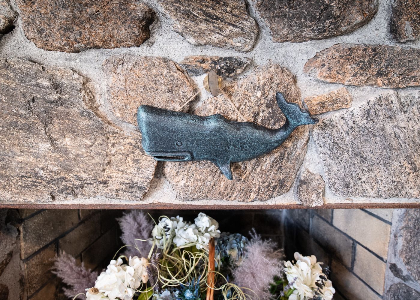A statue of a whale is hanging on a stone wall.
