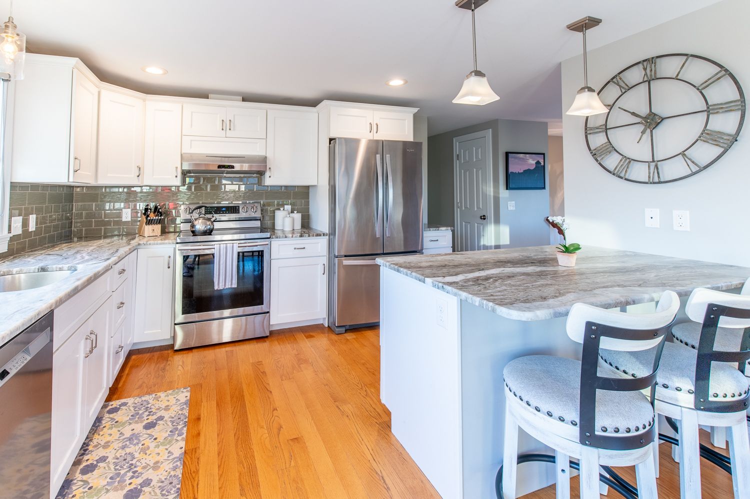 A kitchen with white cabinets and stainless steel appliances and a large clock on the wall.