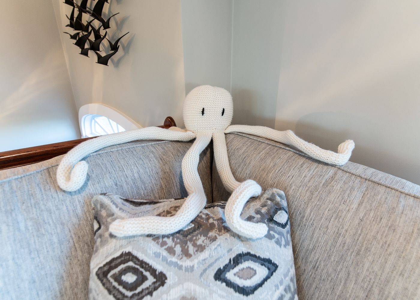 A stuffed octopus is sitting on a pillow on a couch.