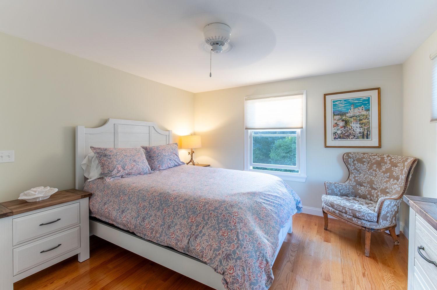 A bedroom with a bed , chair , nightstand and dresser.