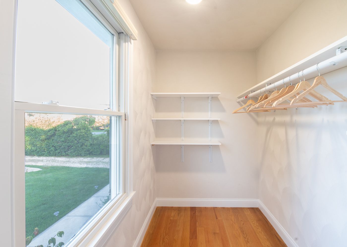 A walk in closet with wooden floors and shelves and a window.