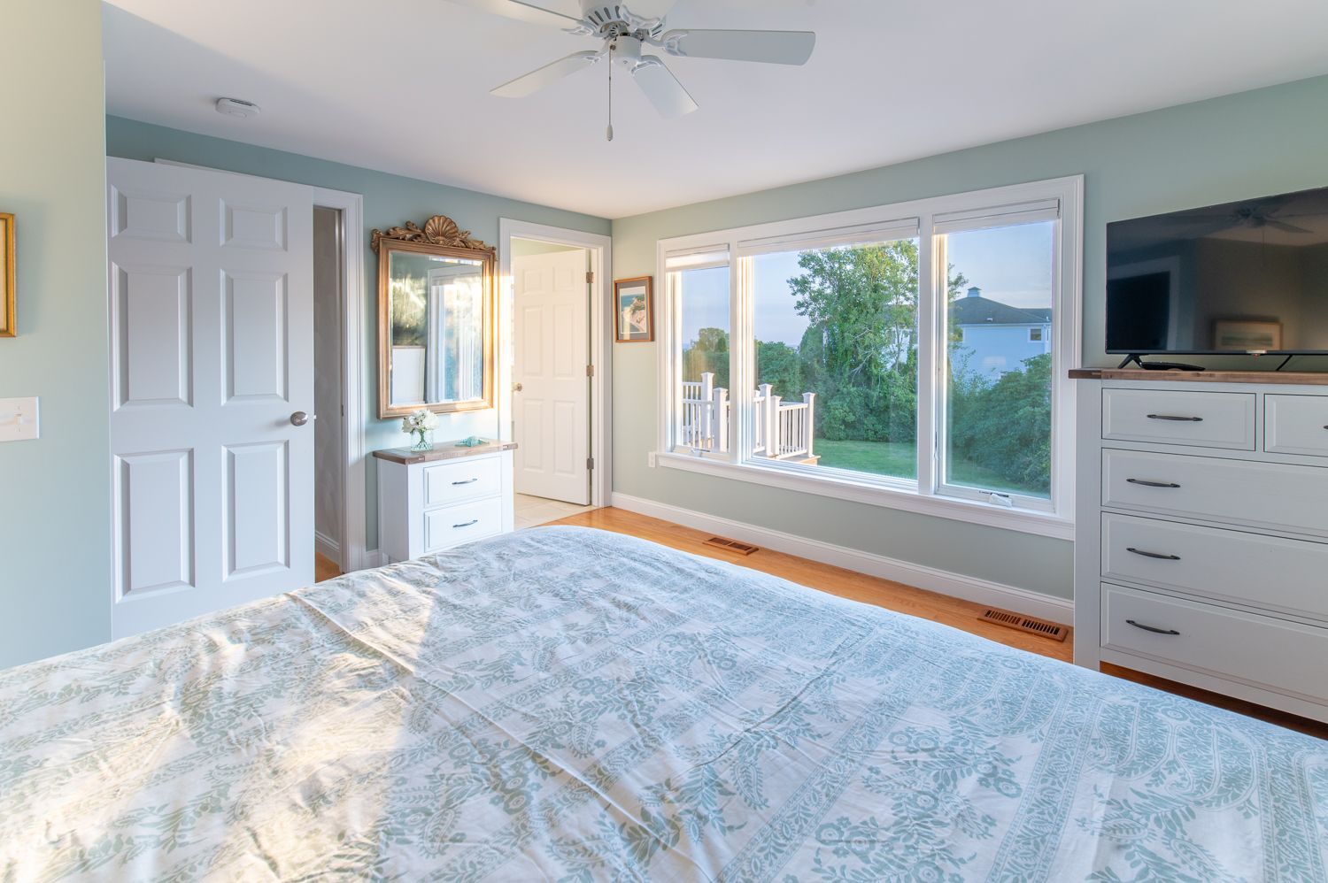 A bedroom with a large bed , a ceiling fan , a television and a large window.