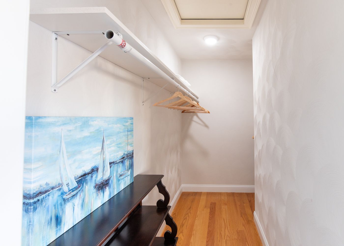 A walk in closet with a painting of sailboats on the wall.