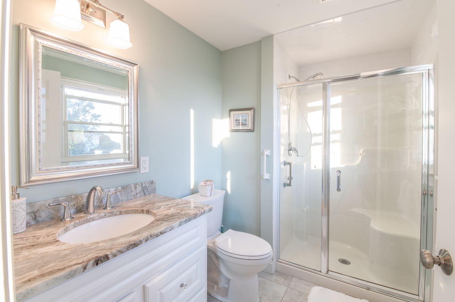 A bathroom with a toilet , sink , mirror and shower stall.
