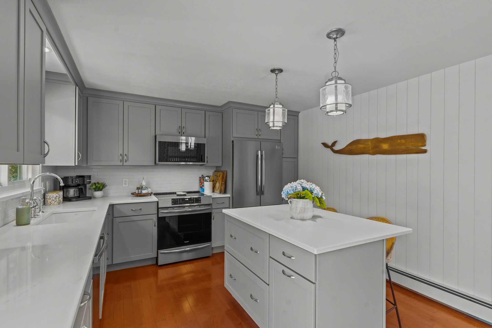 A kitchen with gray cabinets , white counter tops , stainless steel appliances and a large island.