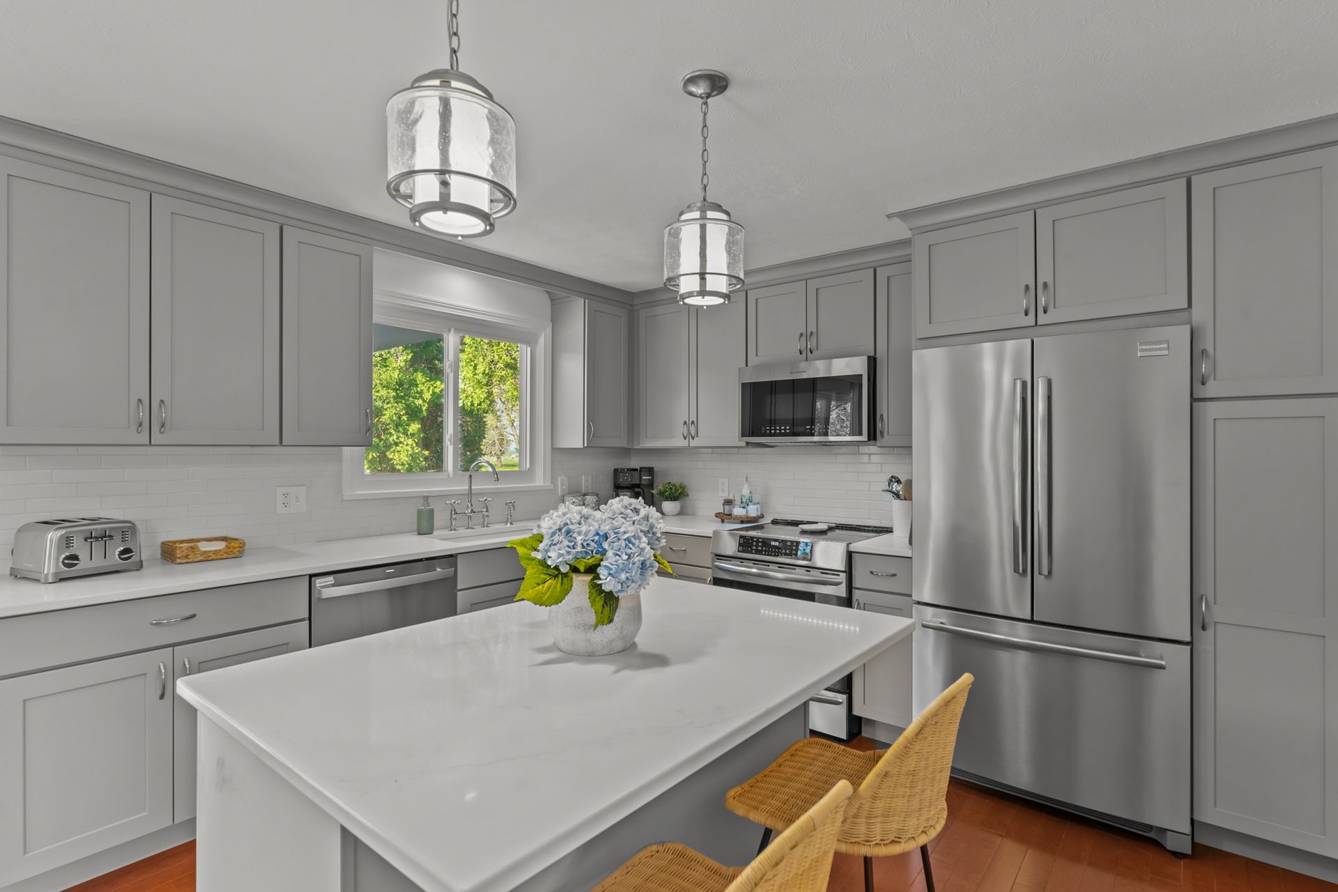 A kitchen with gray cabinets , stainless steel appliances , and a large island.