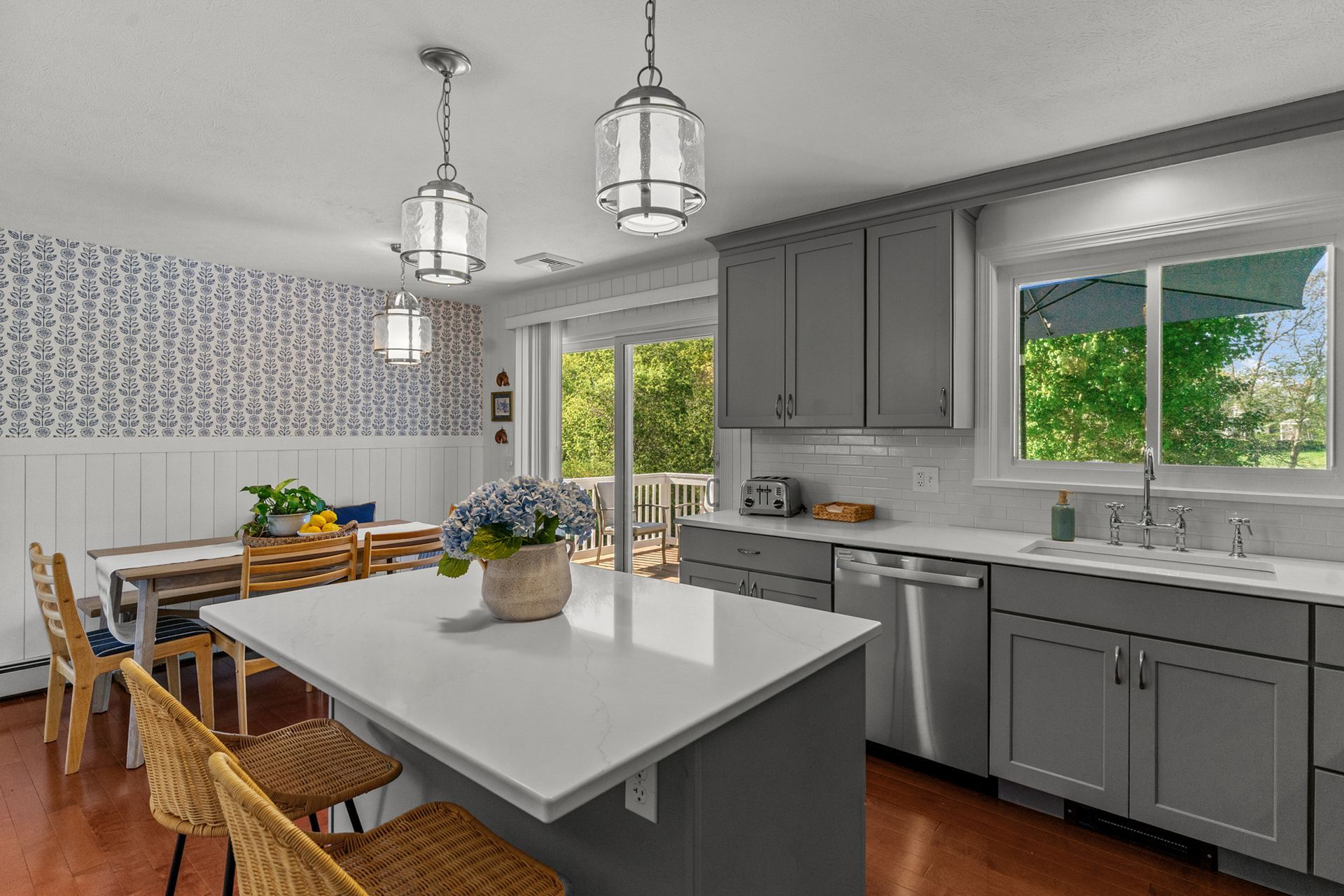 A kitchen with gray cabinets , white counter tops , stainless steel appliances and a large island.