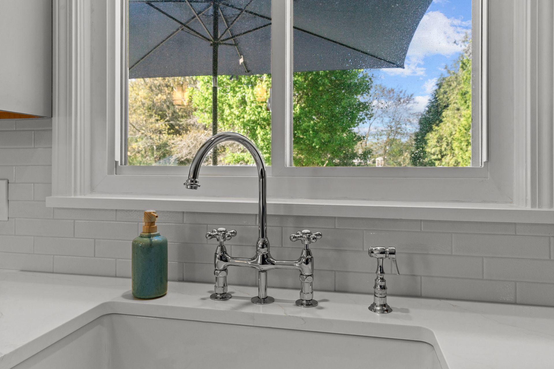 A kitchen sink with a faucet and a window with an umbrella in the background.