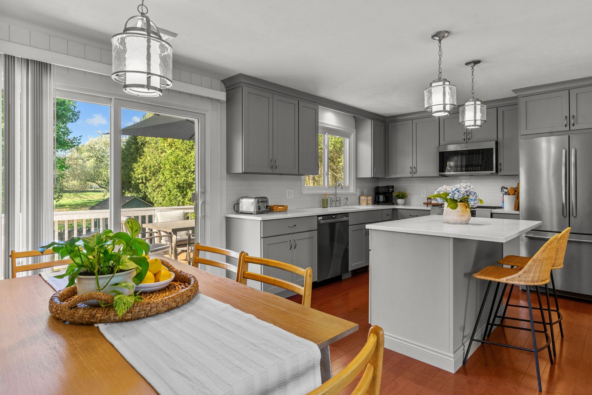 A kitchen with gray cabinets , stainless steel appliances , a large island , a table and chairs.