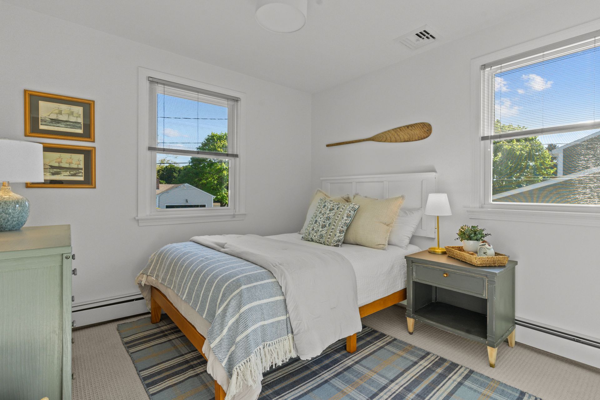 A bedroom with a bed , nightstand , dresser and two windows.