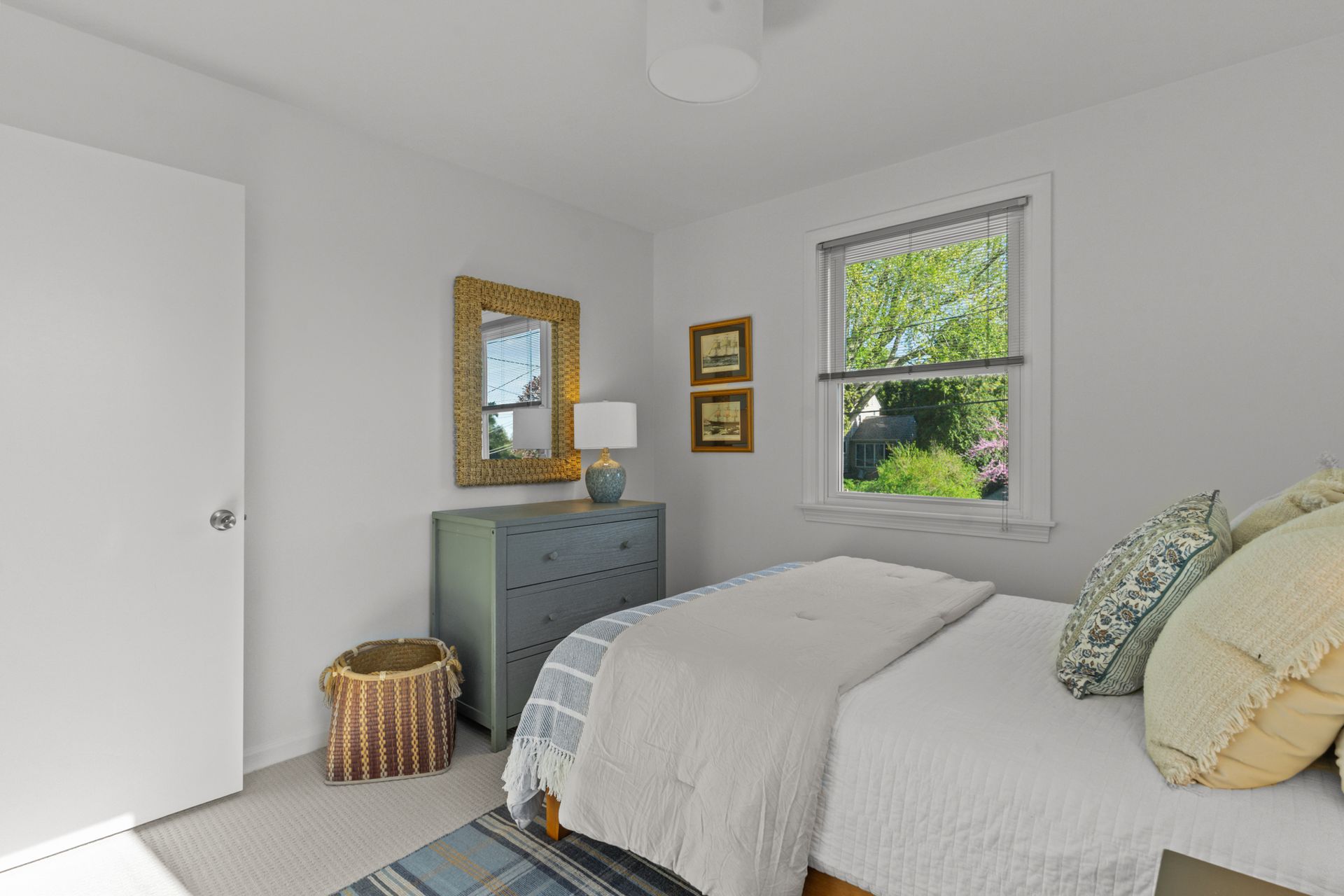 A bedroom with a bed , dresser , mirror and window.
