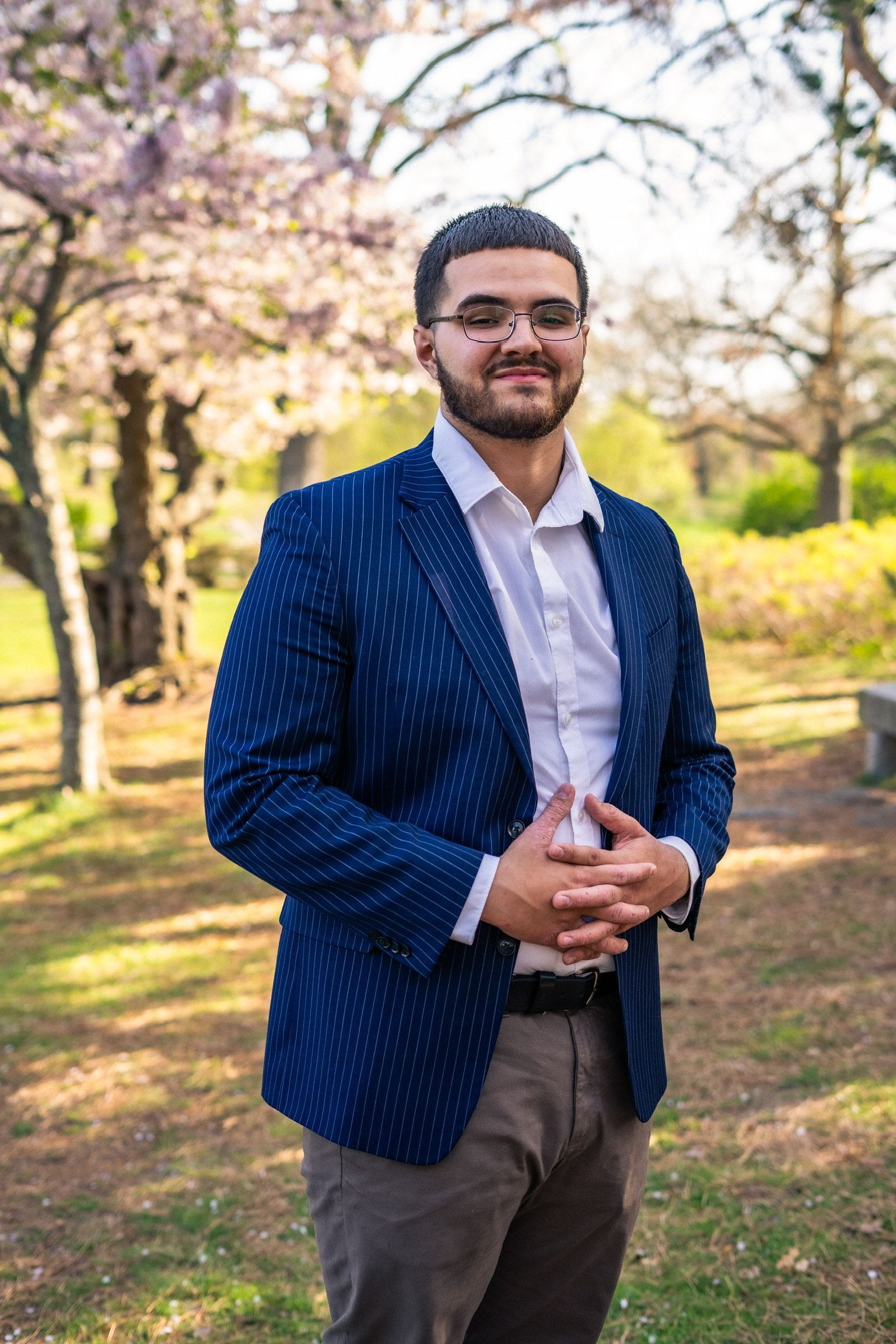 A man in a blue jacket and white shirt is standing in a park.