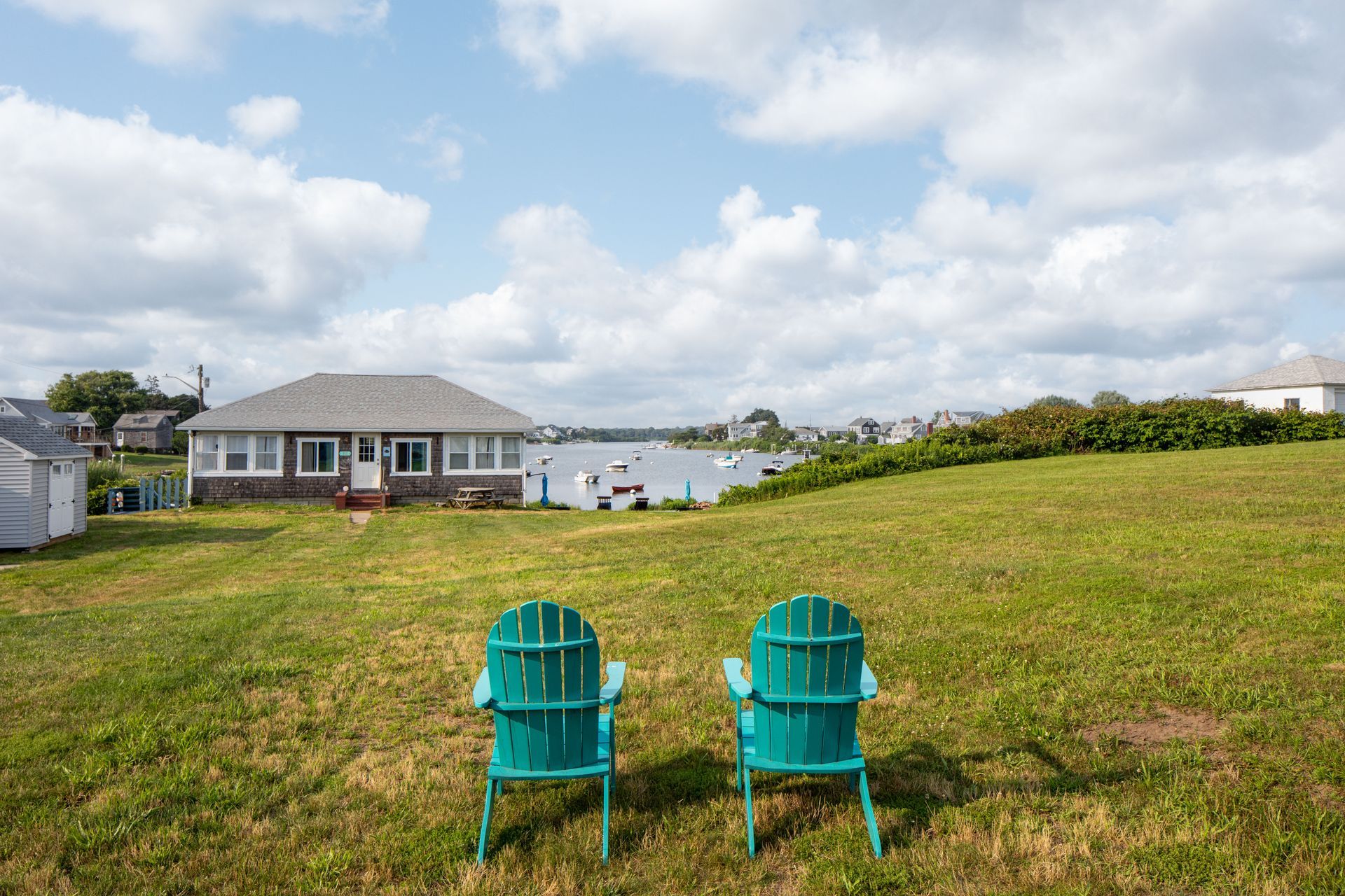 Two green chairs are sitting in a grassy field in front of a house.