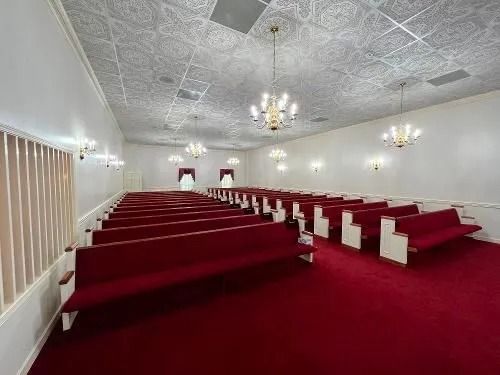 Interior of a funeral home with red carpet, pews, and chandeliers.