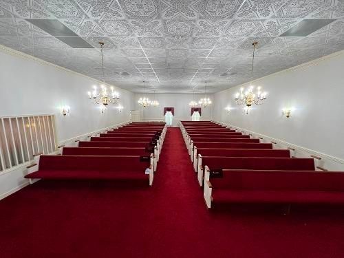 Empty church interior with red carpet, pews, and chandeliers.