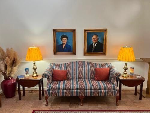 Sofa with framed portraits and lamps on side tables. A vase of dried flowers is to the left.