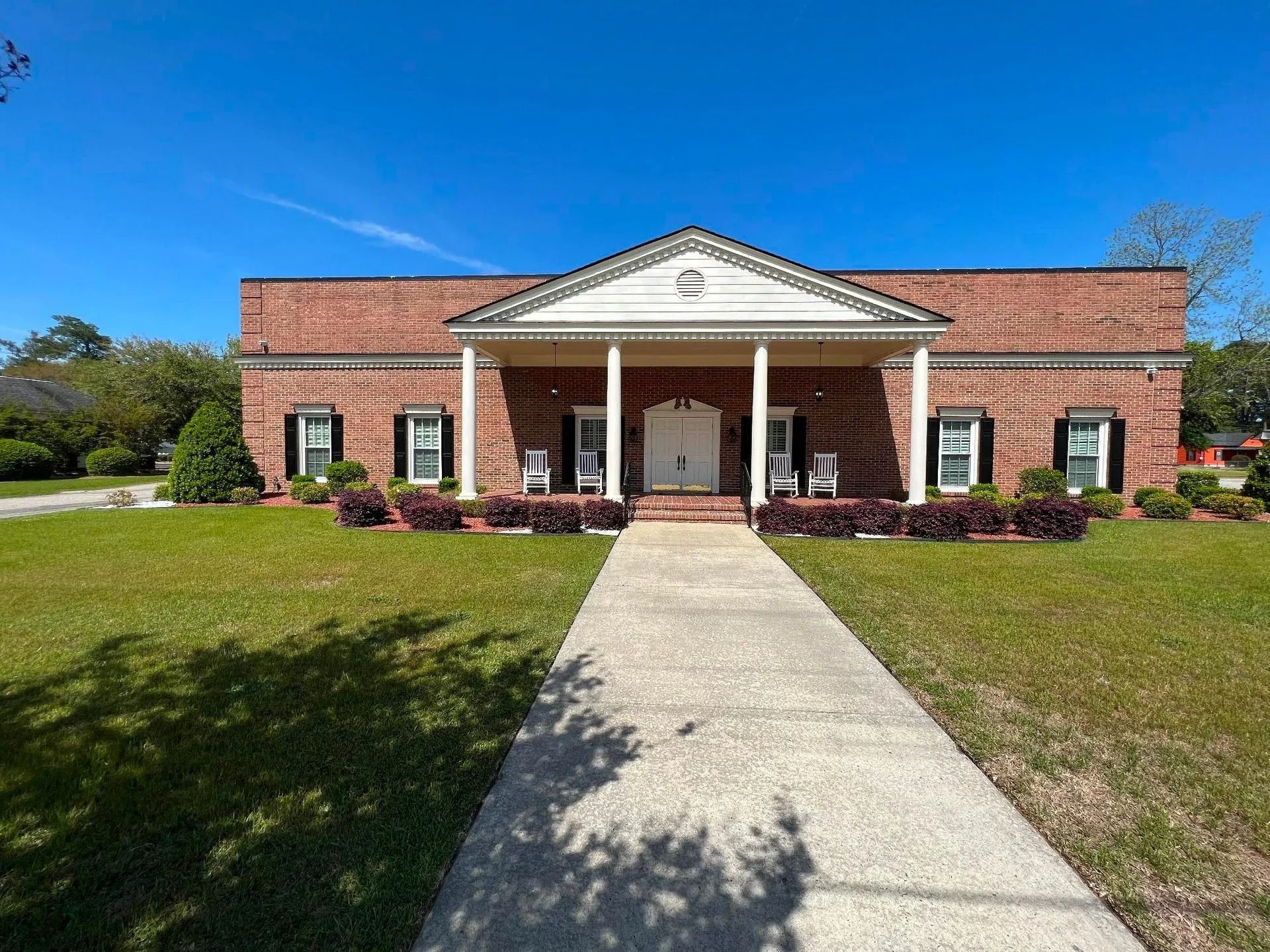 Red brick building with white columns and doors, sidewalk leading from lawn.