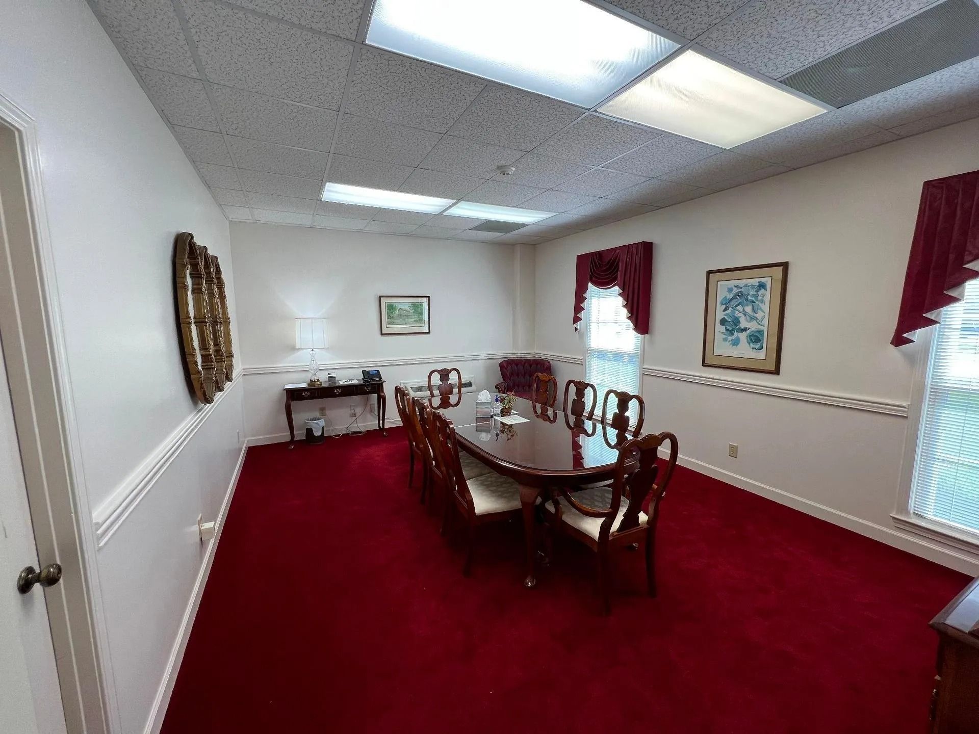 Formal dining room with red carpet, long wooden table, and artwork on cream-colored walls.